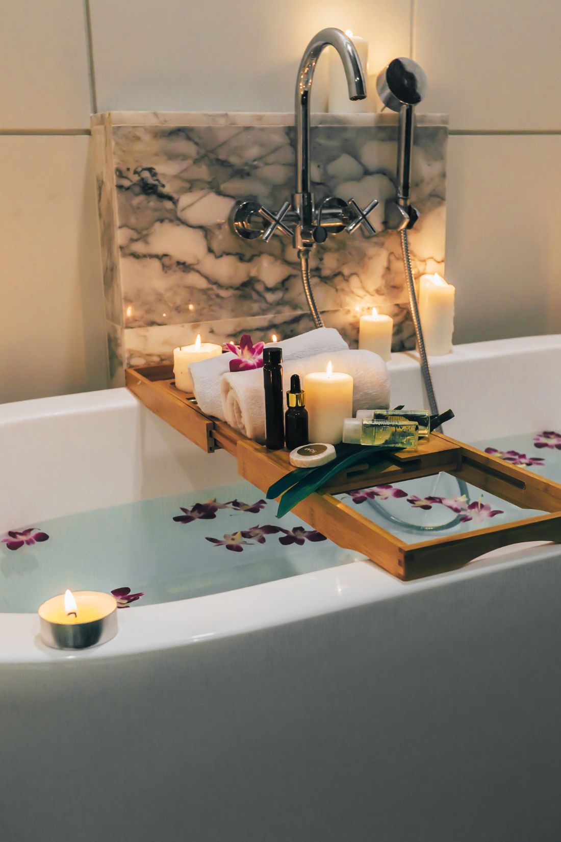 a tray with candles and flowers on the edge of a bathtub